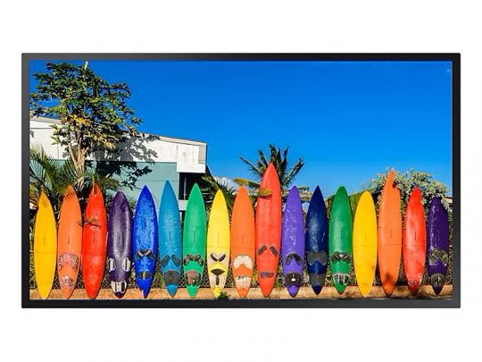 A row of colorful surfboards stands upright in the sand, displayed like eye-catching purchase displays. Behind the surfboards are lush green plants, a small building, and a bright blue sky, creating a vibrant beach scene perfect for surfboard shopping.