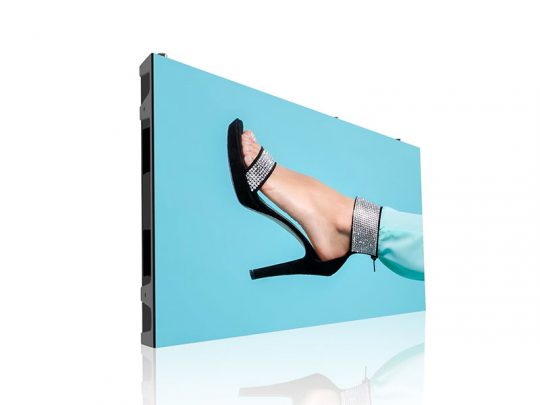 Digital display screen showing a close-up of a foot in a black high-heeled sandal and turquoise pants against a blue background; the screen is angled to the side. Perfect for showcasing footwear or fashion advertisements.