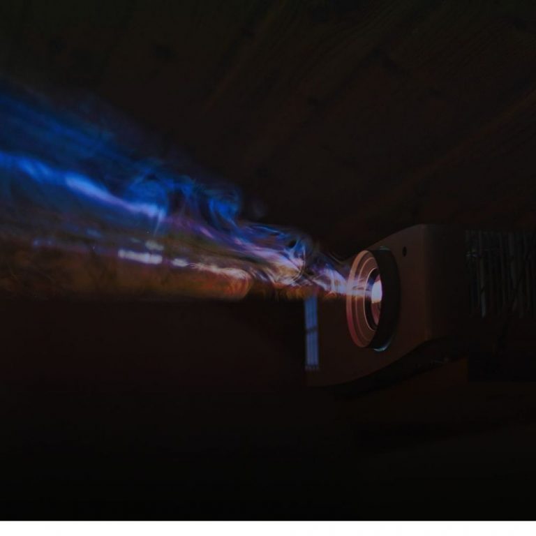 Beamer mieten in Nahaufnahme im dunklen Raum: Der Projektor strahlt leuchtende blaue und violette Lichtstrahlen aus.