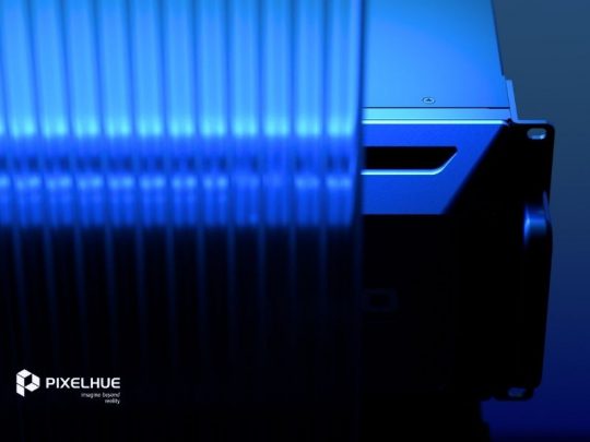 Nahaufnahme eines blau getönten Pixelhue-Geräts hinter Glas, mit "PIXELHUE Innovation - Coming Soon"-Logo unten links.